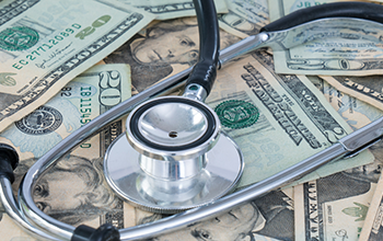 A stethoscope rests on top of scattered U.S. twenty and hundred dollar bills.