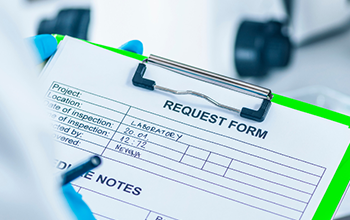 A person in a lab coat holds a clipboard displaying a list of test results in a laboratory setting.